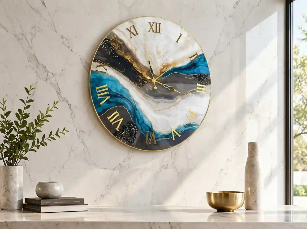 Round wall clock with an abstract blue, black, white, and gold marbled design and gold Roman numerals, mounted on a white marble wall above a marble console with decorative objects.