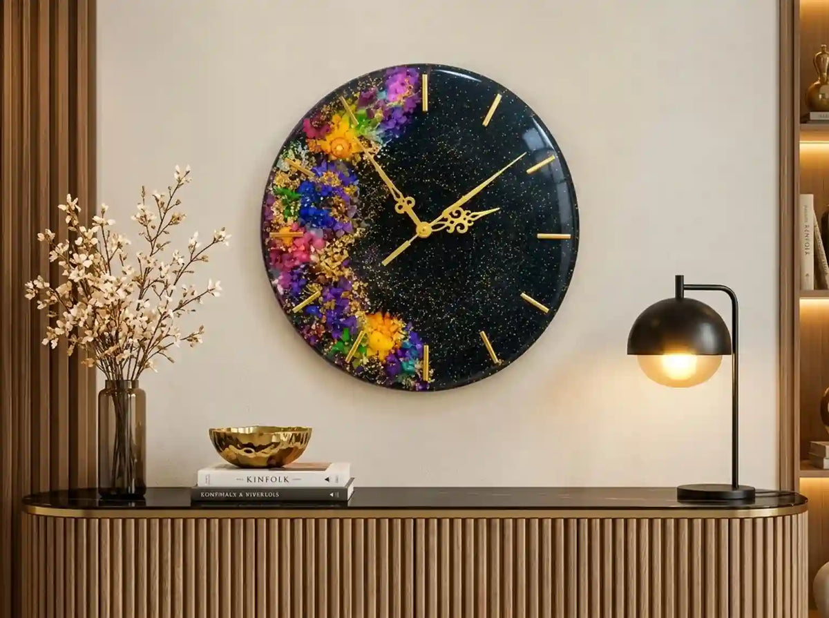 A round wall clock with a black glittery background and a colorful floral design on the left side, styled in a modern home interior above a console table.