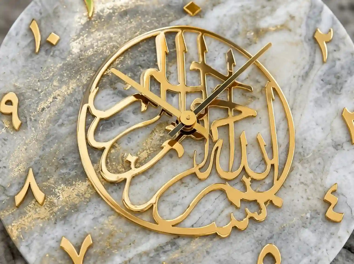 A close-up of a circular gold Islamic wall clock featuring Arabic calligraphy of 'Allah' on a gray and white marble background with gold Arabic numeral cutouts.