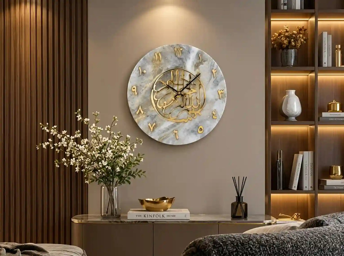 A round wall clock with a white and gray marble pattern, gold Arabic numerals, and a gold central medallion, mounted on a beige wall in a modern, warmly lit living room setting.