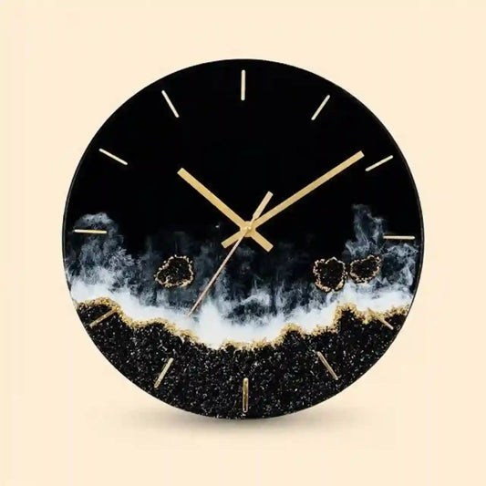 A round wall clock with a black face and frame, featuring gold hands, gold hour markers, and a textured black-and-white geode or smoky wave design near the bottom, shown on a light beige background.